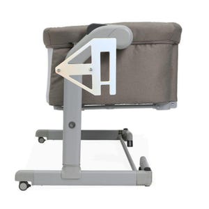 May include: A gray and white baby bassinet with a fabric-covered bed and a metal frame. The bassinet has a white support structure and wheels for easy movement. The bed is covered in a gray fabric.
