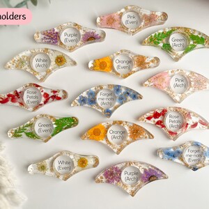 May include: Assortment of 14 handmade resin page holders with pressed flowers and gold glitter. Each page holder is labeled with the type of flower and whether it is an arch or even shape.