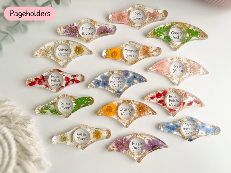 May include: Assortment of 14 handmade resin page holders with pressed flowers and gold glitter. Each page holder is labeled with the type of flower and whether it is an arch or even shape.