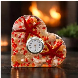 May include: Heart-shaped clock with a clear resin encasing seashells, red starfish, and small red stones. The clock face is white with black numbers and hands. A decorative nautical-themed desk clock.