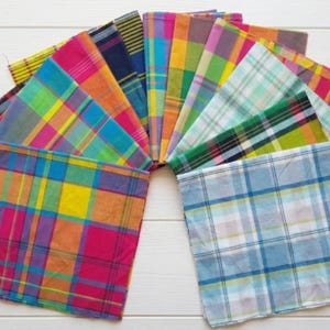 Peut inclure: Une collection de serviettes en tissu carrées disposées en éventail, présentant une variété de motifs à carreaux et écossais vibrants dans des couleurs incluant rose vif, jaune, orange, bleu, vert, violet et blanc, avec des textures tissées.