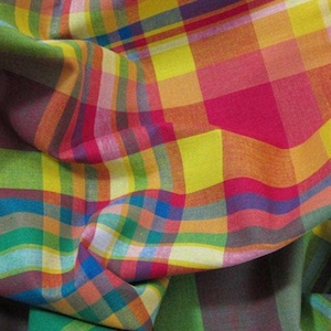 May include: A fabric featuring a vibrant plaid pattern with intersecting lines in bright yellow, hot pink, orange, lime green, and royal blue. The material is gathered into soft folds, highlighting the colorful grid design across the textile surface.