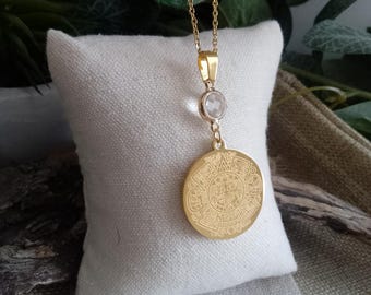 May include: Gold necklace with a round pendant featuring an intricate design and a clear crystal accent.