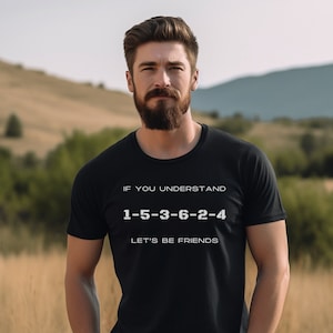 May include: A black t-shirt with white text that reads "If you understand 1-5-3-6-2-4 Let's be friends". The shirt is being worn by a person with a beard standing in a field.