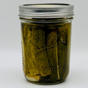 May include: A glass jar filled with green dill pickles, with a silver lid and the word "Ball" printed on the side.