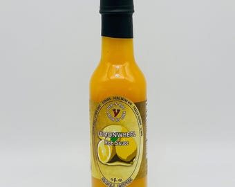 Op de afbeelding: Een doorzichtige glazen fles gevuld met felgele hete saus, afgesloten met een zwarte dop. Het etiket bevat de tekst Lemonwheel Hot Sauce, Deb-A-Roo Labor of Love en 5 fl. oz., met illustraties van gele citroenen en chilipepers.