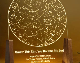 Może przedstawiać: Spersonalizowana lampka nocna z okrągłym wzorem mapy gwiazd. Posiada drewnianą podstawę i wyświetla tekst "Under This Sky, You Became My Dad", a także datę, godzinę i lokalizację.