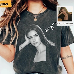 May include: Dark gray t-shirt featuring a black and white portrait of a person. The shirt has a vintage wash look. A small photo with the text "UPLOAD PHOTO" is on the right side of the shirt. The word "Pepper" is in a yellow rectangle.