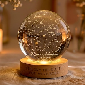 May include: A glowing glass sphere displaying a constellation map, personalized with the name "Marie Johnson", date "April 20, 2003", and location "Los Angeles, CA". The sphere sits on a wooden base engraved with "THE SKY THE NIGHT YOU WERE BORN".