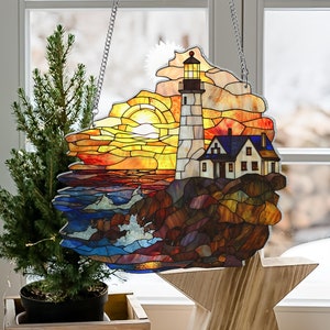 May include: A stained glass window hanging with a colorful depiction of a lighthouse on a rocky shore with a sunset in the background.