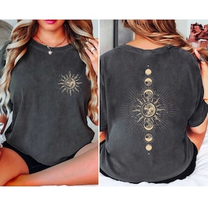 May include: A charcoal gray t-shirt with a sun and moon design. The front of the shirt features a sun with a face, and the back of the shirt features a sun with a face and a crescent moon.