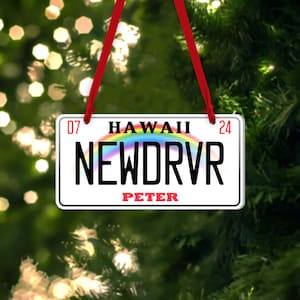 Puede incluir: Adorno navide&ntilde;o blanco y rojo con forma de matr&iacute;cula de Haw&aacute;i con el texto "HAWAII 07 NEWDRVR 24" y el nombre "PETER" debajo.