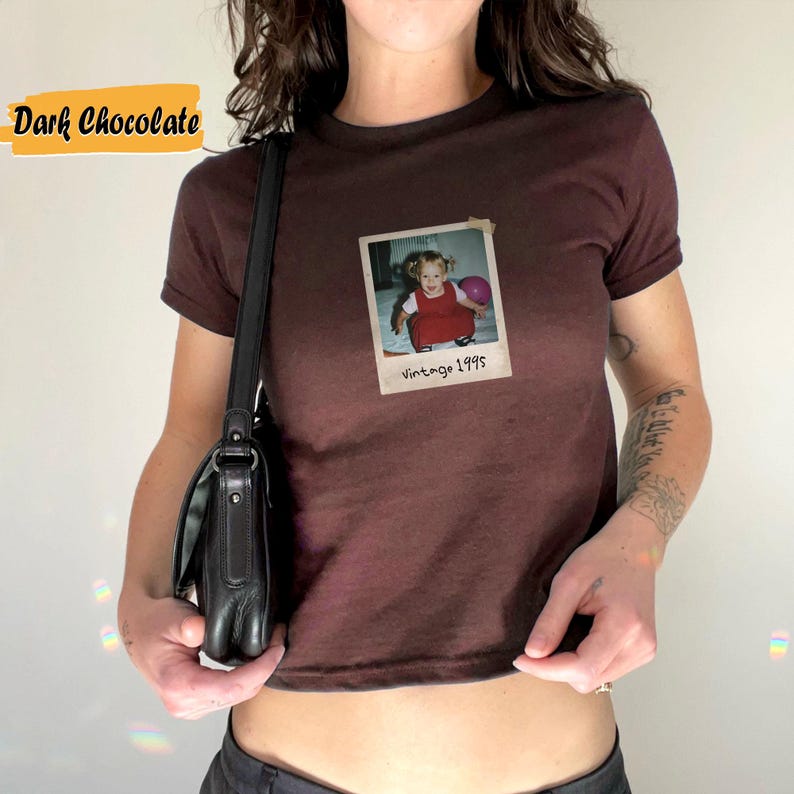 Peut inclure: Un t-shirt court de couleur chocolat fonc&eacute; avec une photo vintage d'une jeune fille tenant un ballon rose. La photo est encadr&eacute;e d'une bordure blanche et porte le texte "Vintage 1995" en dessous.
