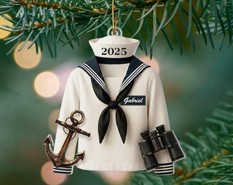 May include: A nautical-themed Christmas ornament featuring a sailor's uniform with the year "2025" on the hat and the name "Gabriel" on a patch. Includes a bronze anchor and black binoculars. The ornament is hanging from a gold string.
