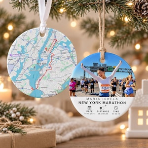 Puede incluir: Dos adornos redondos de cerámica colgados de cintas. Uno muestra un mapa de Nueva York con una ruta roja. El otro muestra a una corredora cruzando la meta con el texto MARIA ISBELA NEW YORK MARATHON, 10.10.2026, 26.2 MILES, 03:50:10.