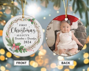 May include: A personalized Christmas ornament with a photo on one side and festive text on the other. The front features a wreath design with the words "First Christmas" and the year 2024. The back displays a baby in a white dress.