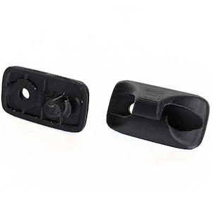 May include: Two black plastic components, likely 3D-printed, are displayed against a white background. One component is rectangular with a circular hole and a protruding knob. The other has a curved design with a hole and a recessed area.