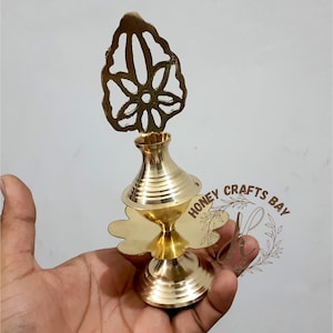 Pode incluir: Uma lâmpada de óleo de metal dourado com um design floral decorativo na parte superior. A lâmpada tem uma base redonda e um pequeno bico para verter óleo.