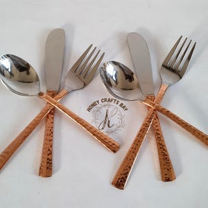 May include: A set of silverware including spoons, knives, and forks. The utensils have shiny silver heads and copper-colored hammered handles. The image shows two sets of silverware, each set consisting of a spoon, knife, and fork.