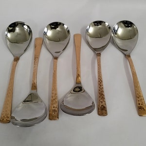 Puede incluir: Juego de seis cucharas y utensilios de servir de acero inoxidable. Las cucharas tienen un cuenco plateado pulido y mangos de color cobre. Los mangos tienen una textura martillada. El utensilio de servir tiene un cuenco triangular y un mango de cobre.