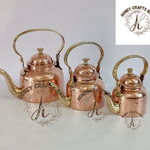 Puede incluir: Tres teteras de cobre con superficies martilladas y asas de latón. Las teteras están dispuestas en orden de tamaño, de la más grande a la más pequeña.