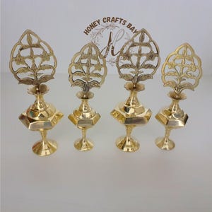 Puede incluir: Conjunto de cuatro botellas decorativas de metal dorado con intrincados diseños florales en la parte superior. Las botellas tienen una base hexagonal y un cuerpo redondo. Las botellas están sobre una superficie blanca.  "Honey Crafts Bay" está escrito en la parte superior de la imagen.