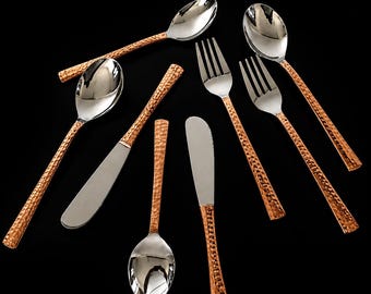 May include: A set of flatware featuring polished silver-tone heads and textured copper-colored handles. The collection includes three spoons, two forks, and two knives, all arranged against a solid black background to highlight the metallic contrast.