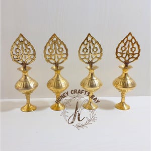 Peut inclure: Quatre flacons de parfum décoratifs en laiton antique. Chaque flacon a un corps bulbeux, un col fin et un dessus décoratif en forme de feuille. Les flacons sont disposés en rangée sur une surface blanche. Le texte "HONEY CRAFTS BAY" est visible.