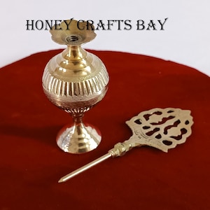 May include: A gold metal bottle with a decorative top and a matching metal applicator. The bottle is on a red velvet surface.