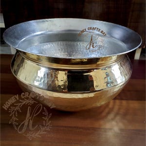 Op de afbeelding: Een gehamerde messing kom met een brede, zilverkleurige rand. De kom heeft een afgeronde body en een getextureerd oppervlak. De woorden "HONEY CRAFTS BAY" zijn zichtbaar op de kom. Deze decoratieve kom is geschikt om te serveren of tentoon te stellen.