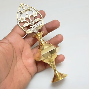 Pode incluir: Um frasco de perfume dourado com um tampão floral. O frasco tem um corpo geométrico facetado e uma base alargada. O tampão apresenta um design vazado de flores e folhas. Feito de metal.
