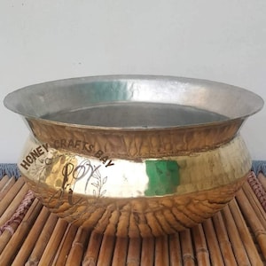 May include: A hammered brass bowl with a silver rim. The bowl has a textured surface and is sitting on a bamboo mat.