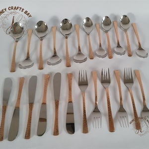 Puede incluir: Un juego de 24 cubiertos de cobre martillado y acero inoxidable, que incluye cucharas, tenedores y cuchillos para mantequilla. Los mangos son de color cobre y los cubiertos son plateados.