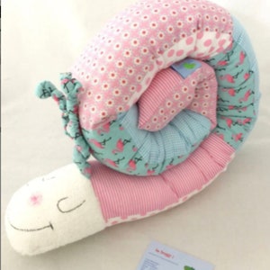 Könnte beinhalten: Ein rosa-blaues Patchwork-Schnecken-Plüschtier mit weißem Gesicht und einem lächelnden Mund. Die Schnecke ist spiralförmig zusammengerollt.