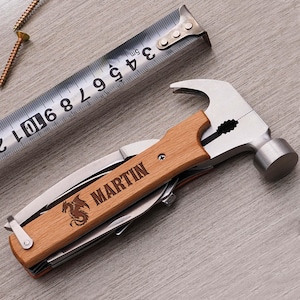 May include: A multi-tool hammer with a wooden handle, featuring a knife, pliers, and other tools. The handle is engraved with the name "MARTIN" and a dragon emblem. A metal tape measure and screws are also visible.