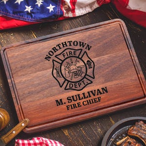 May include: A rectangular dark brown wooden cutting board featuring a laser-engraved fire department emblem with a ladder, helmet, and hydrant. The text reads NORTHTOWN FIRE DEPT. and M. SULLIVAN FIRE CHIEF in bold black lettering.