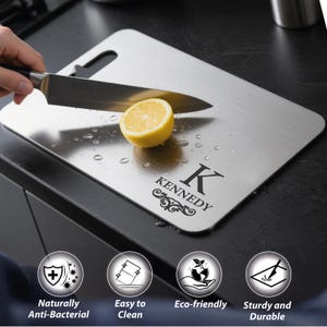 May include: A stainless steel cutting board with a lemon half and a knife. The board has a handle and is engraved with the name "KENNEDY" and a decorative initial "K". The board is labeled as naturally anti-bacterial, easy to clean, eco-friendly, and sturdy.