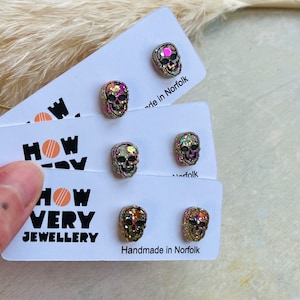 May include: A set of four pairs of glitter skull stud earrings. The earrings are on white cards with the text "How Very Jewellery" and "Handmade in Norfolk".