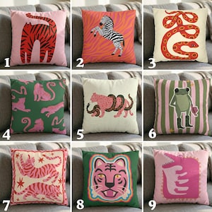 May include: Collection of decorative throw pillows with animal designs. Pillows feature a tiger, zebra, snake, leopard, frog, and crocodile. The pillows have pink, green, orange, and white backgrounds. The animal illustrations are in a cartoon style.