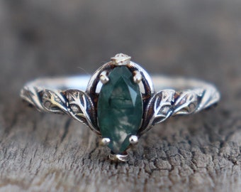 Peut inclure: Une bague en argent avec une pierre précieuse verte sertie dans un motif de feuilles.