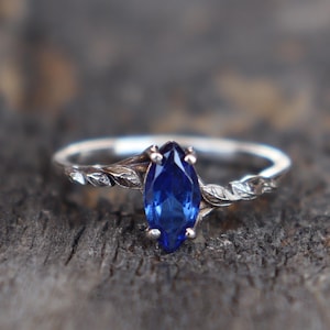 May include: A silver ring with a blue marquise-shaped gemstone set in a twisted band.