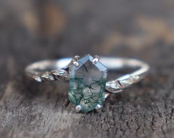 Peut inclure: Une bague en argent avec une pierre précieuse en agate mousse verte sertie dans une bande torsadée.