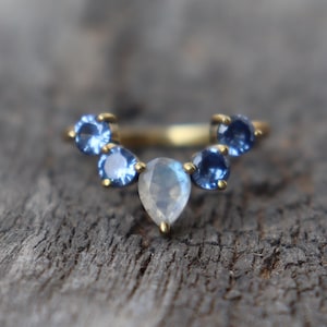 May include: A gold ring with a pear-shaped moonstone and five smaller blue sapphires set in a curved band.