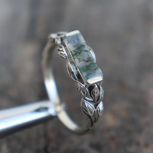 Puede incluir: Un anillo de plata con una piedra de ágata verde musgo engastada en un diseño de hojas.