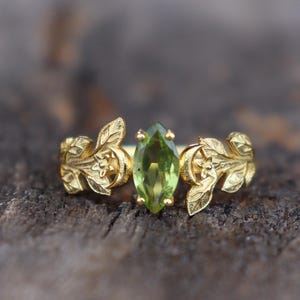 以下が含まれることがあります： 葉のデザインにセットされた緑色の宝石が付いた金の指輪です。