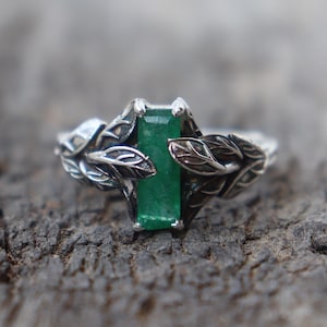 May include: A silver ring with a green emerald gemstone set in a leaf design.