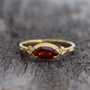 May include: A gold ring featuring a red gemstone set in a marquise shape. The ring has a delicate floral design on the band.
