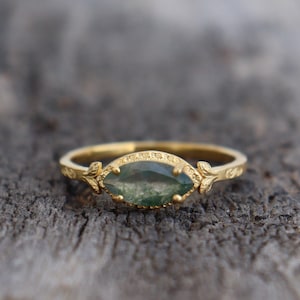 Può includere: Un anello d'oro con una pietra preziosa verde incastonata a forma di marquise. L'anello presenta un delicato motivo floreale sulla fascia.