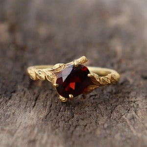 Può includere: Un anello d'oro con una pietra preziosa rossa incastonata in un design a forma di foglia.