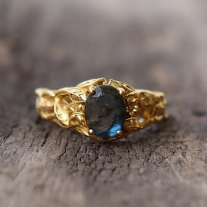 Puede incluir: Un anillo de oro con una piedra preciosa azul engastada en un diseño de hojas.